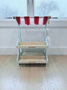Wooden toy kitchen with red and white striped canopy on a light wooden floor.