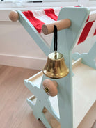 Gold bell attached to a light blue stand with wooden handles on a wooden floor.