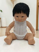 Baby doll with black hair wearing a white lace romper on a light background