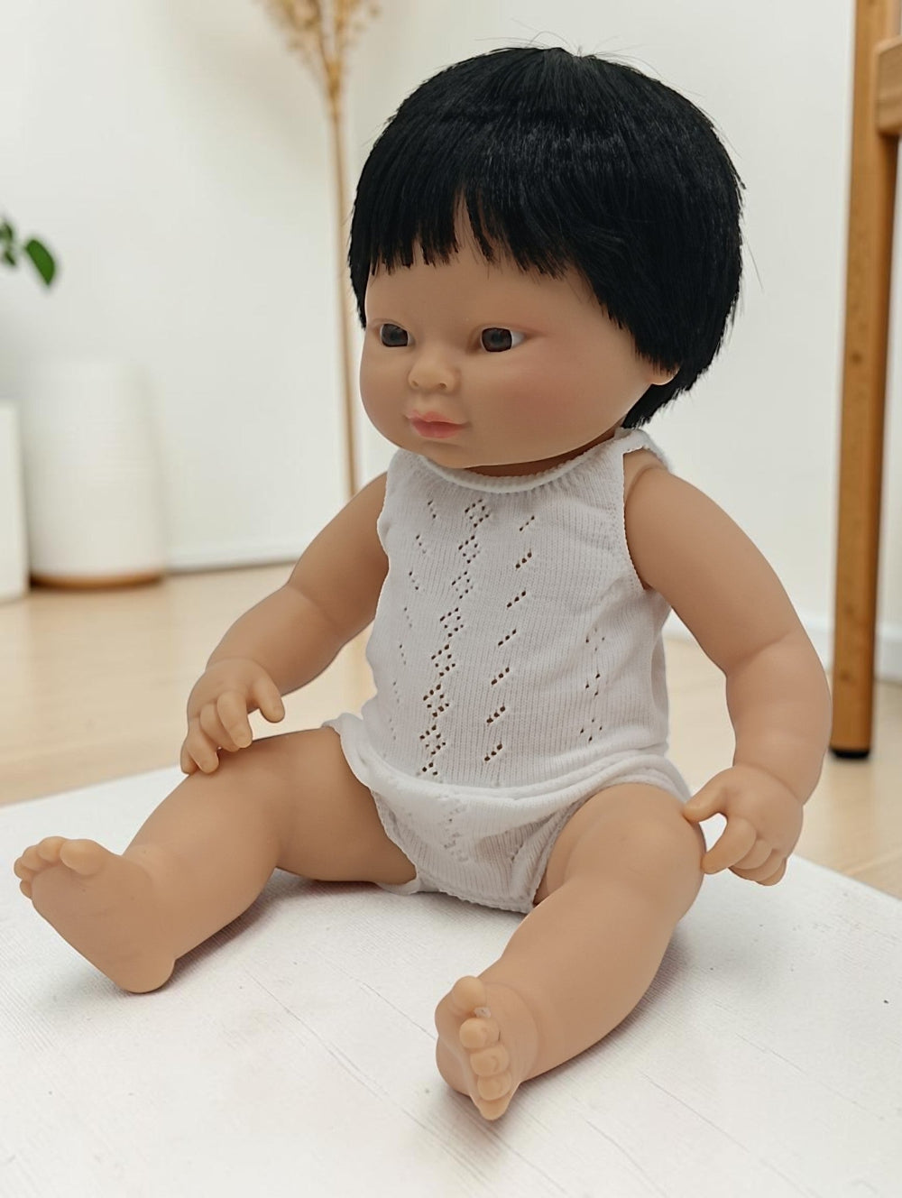 Doll with black hair wearing a white sleeveless top and diaper on a light surface.