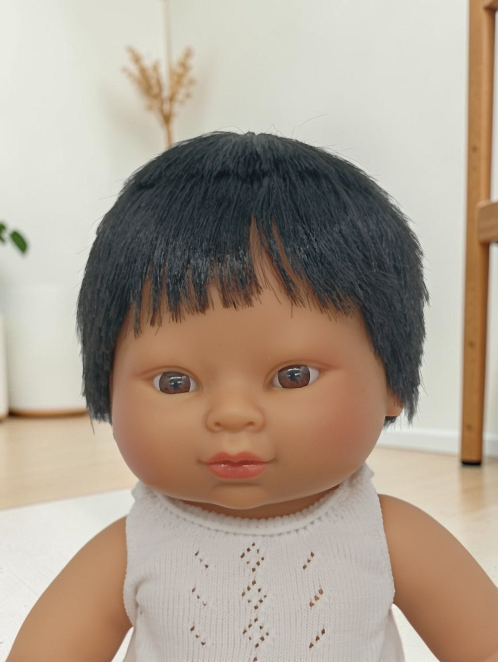 Doll with black hair and a white outfit against a neutral background
