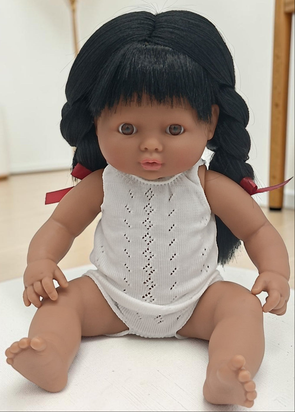 Doll with black hair in pigtails wearing a white outfit on a light background
