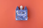 Blue castle-shaped box with a white plush toy on an orange background