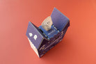 Small plush toy inside a purple box on an orange background