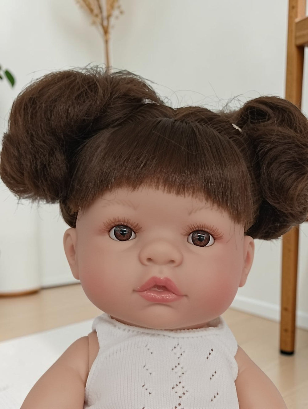 Baby doll with brown hair styled in buns wearing a white outfit.