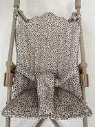 A fabric stroller seat liner with a small-scale floral print in muted pink, green, and purple on an off-white background, shown fitted over a stroller frame.