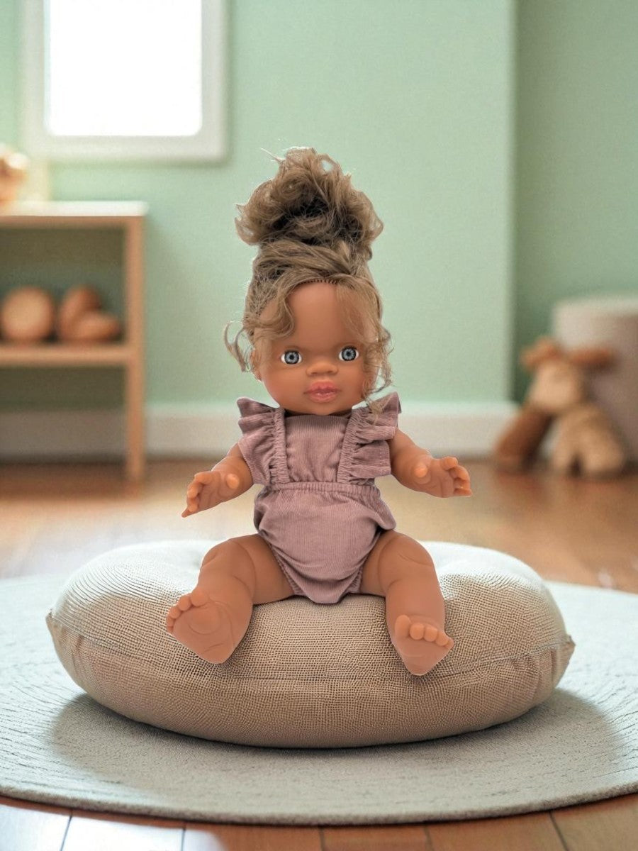 Doll sitting on a cushion in a room with a green wall and wooden floor.