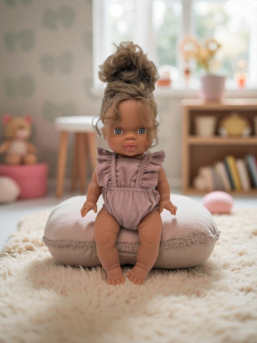 Doll in a chestnut outfit sitting on a cushion in a room with toys and books.