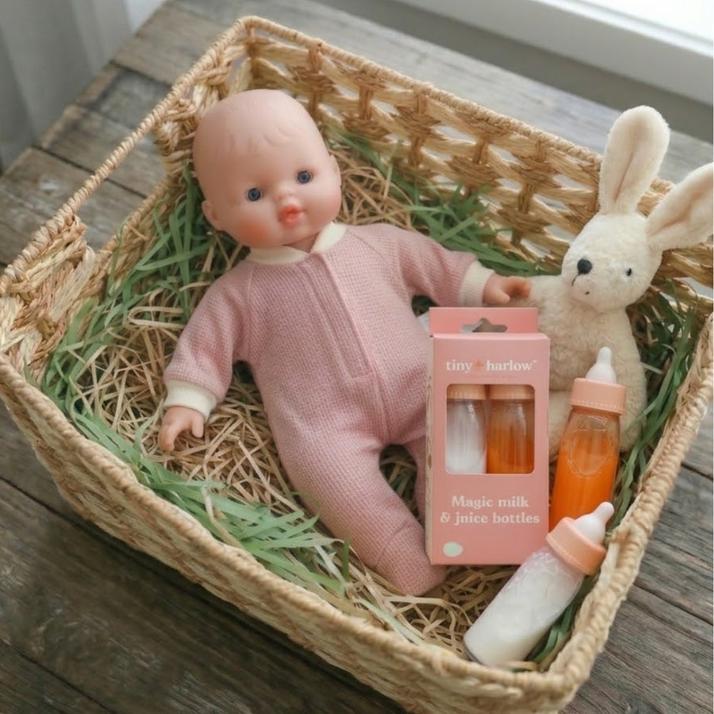 Toy doll in a pink outfit with bottles and a rabbit plush toy in a woven basket.
