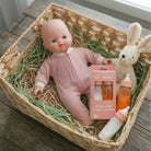 Toy doll in a pink outfit with bottles and a rabbit plush toy in a woven basket.