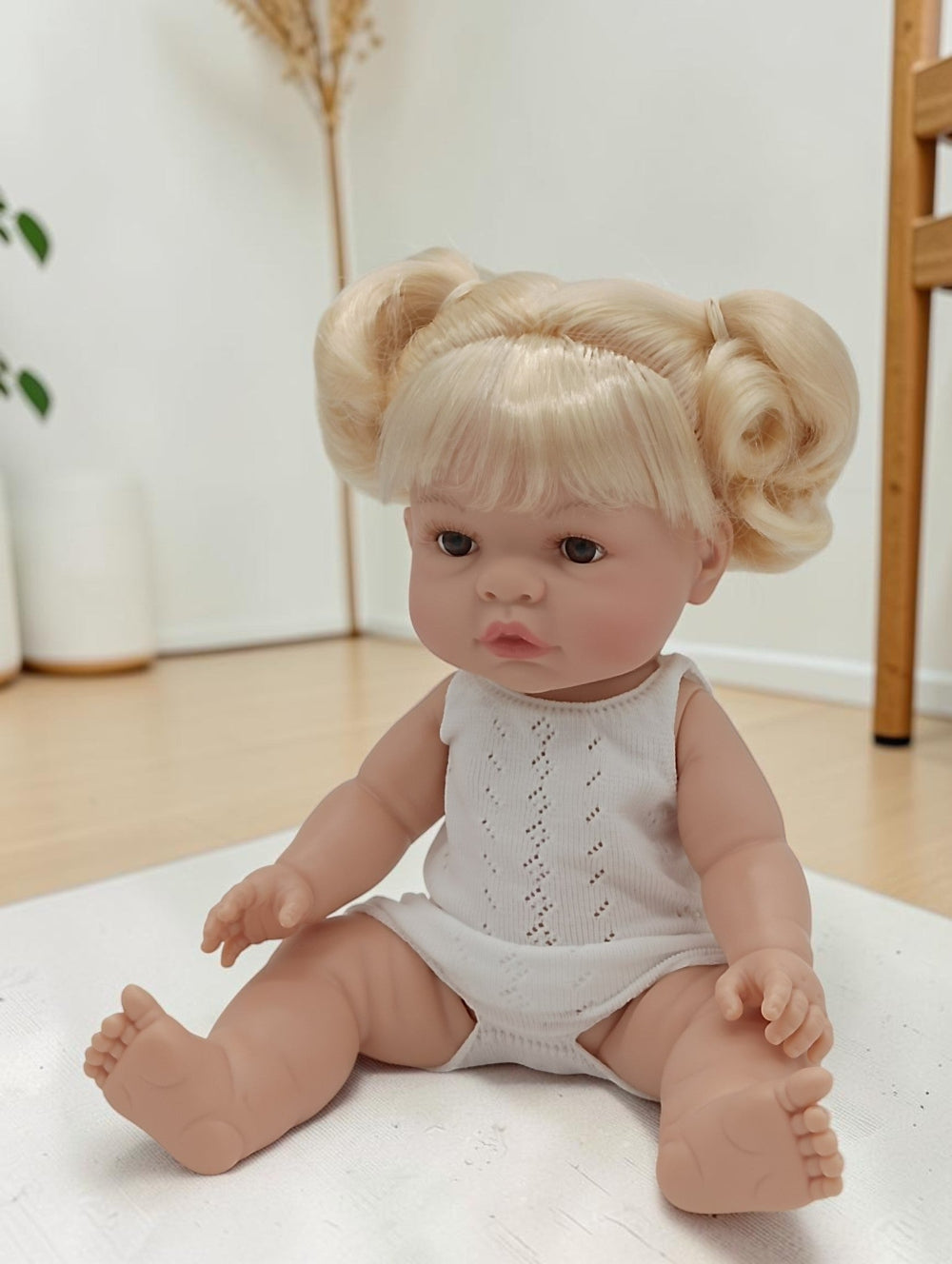 Baby doll with blonde hair styled in pigtails sitting on a white surface.