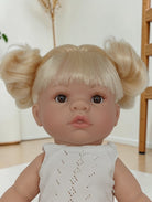 Baby doll with blonde hair styled in pigtails wearing a light gray dress indoors.