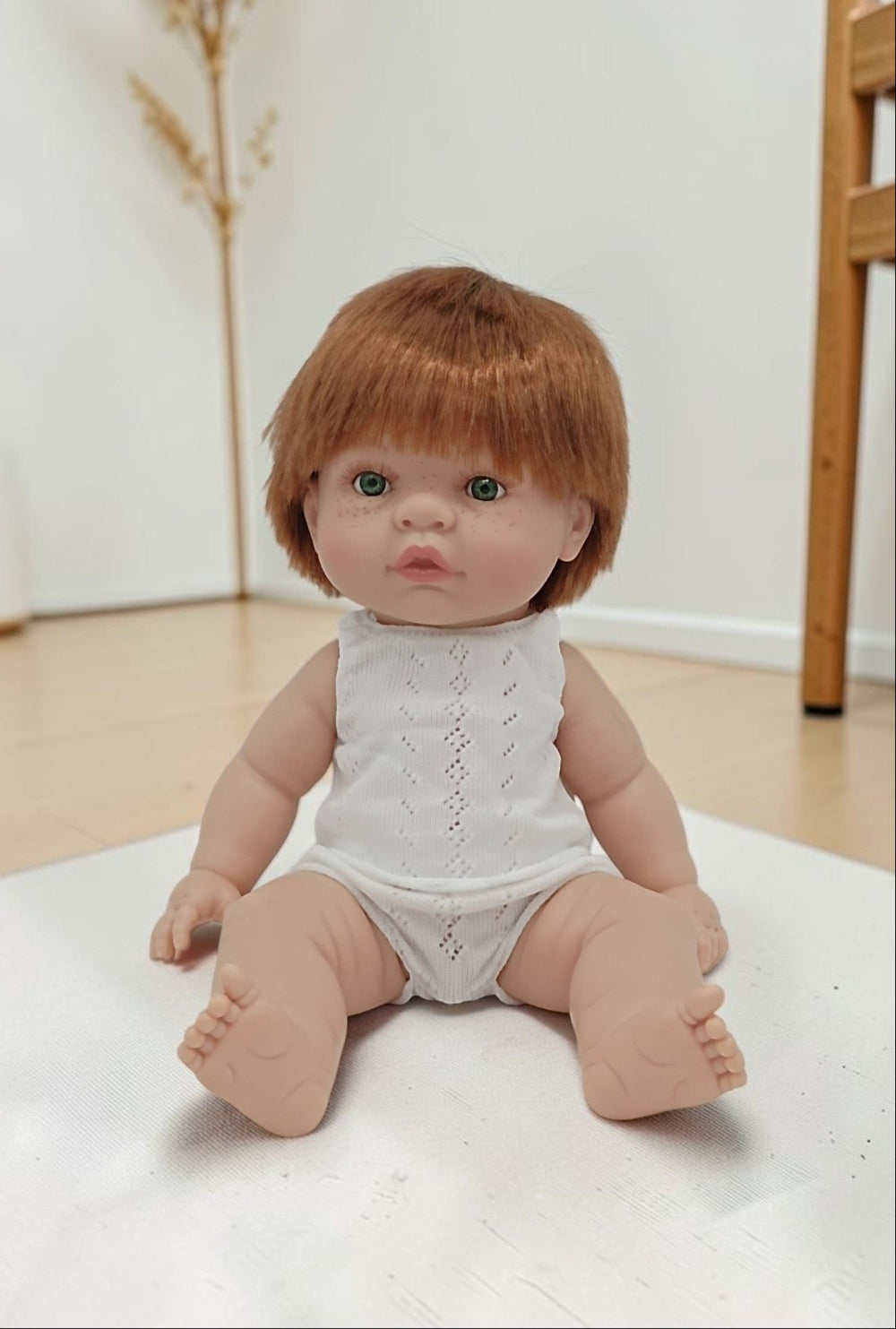 Baby doll with red hair wearing a white lace romper on a light surface.