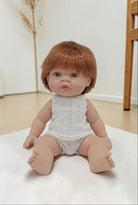 Baby doll with red hair wearing a white lace romper on a light surface.