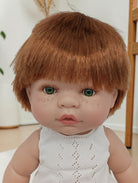 Realistic doll with brown hair and freckles wearing a white sleeveless top.