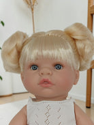 Doll with blonde hair styled in pigtails and blue eyes wearing a white top.