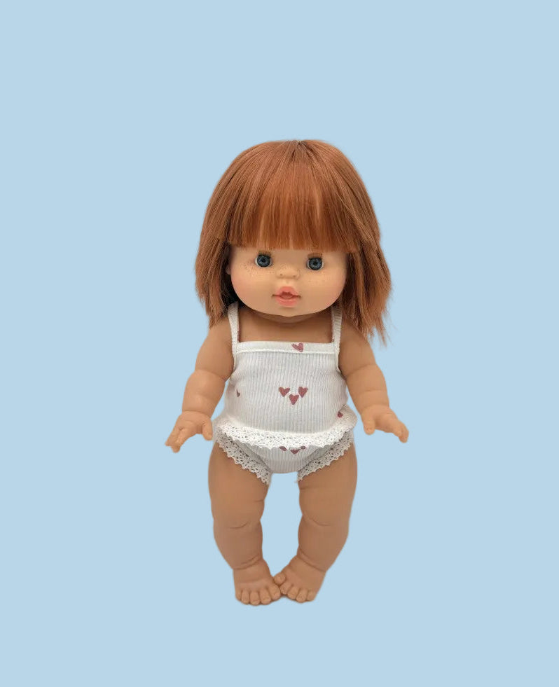 Doll with brown hair wearing a white outfit with red hearts on a light gray background