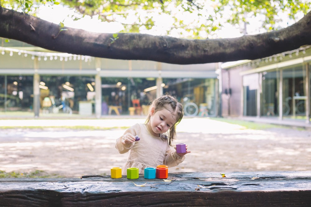 Child playing with colorful blocks on a wooden surface outdoors