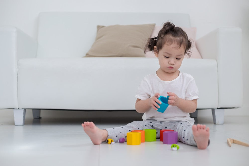 Child playing with colorful blocks on a white floor in front of a white couch.