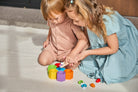 Two young girls playing with colorful building blocks on a light surface.