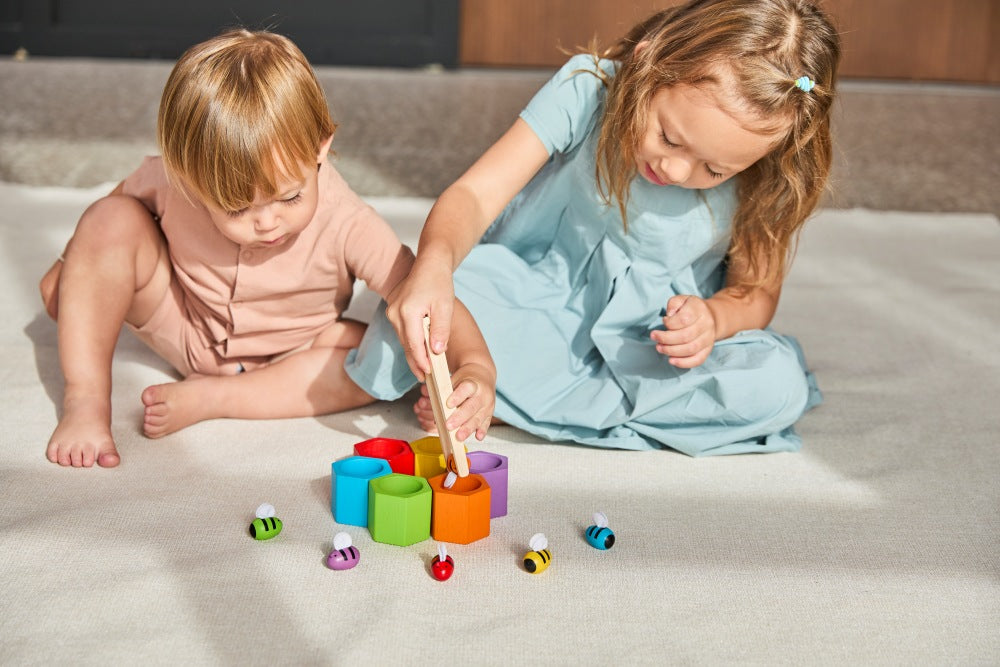 Two children playing with colorful toys on a light-colored surface.