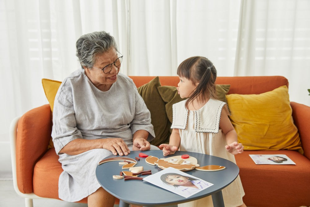 Grandparent and granddaughter sitting on an orange couch with a small round table in front of them.