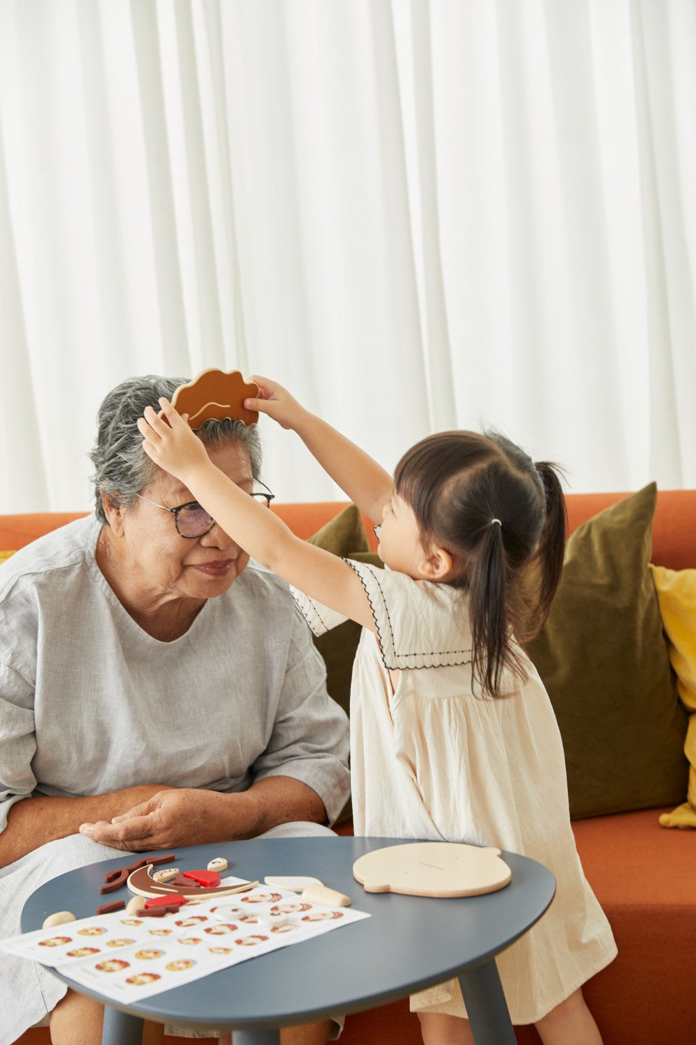 Grandparent and granddaughter playing with a wooden toy on a couch