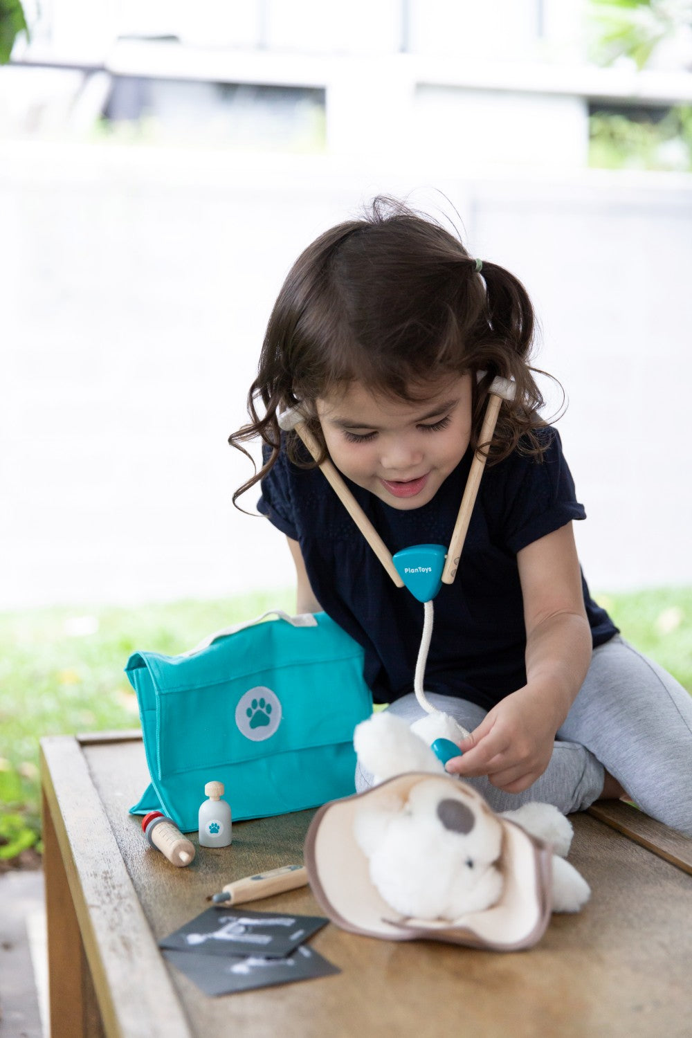 Child playing with a toy doctor set on a wooden table outdoors.