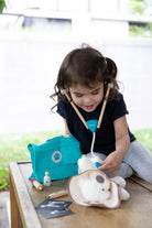 Child playing with a toy doctor set on a wooden table outdoors.