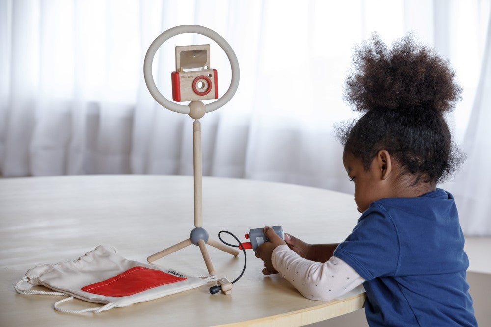 Child playing with a toy camera on a stand in a bright room