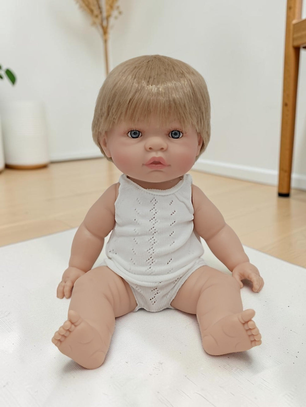 Realistic baby doll with blonde hair and blue eyes wearing a white outfit on a light surface.