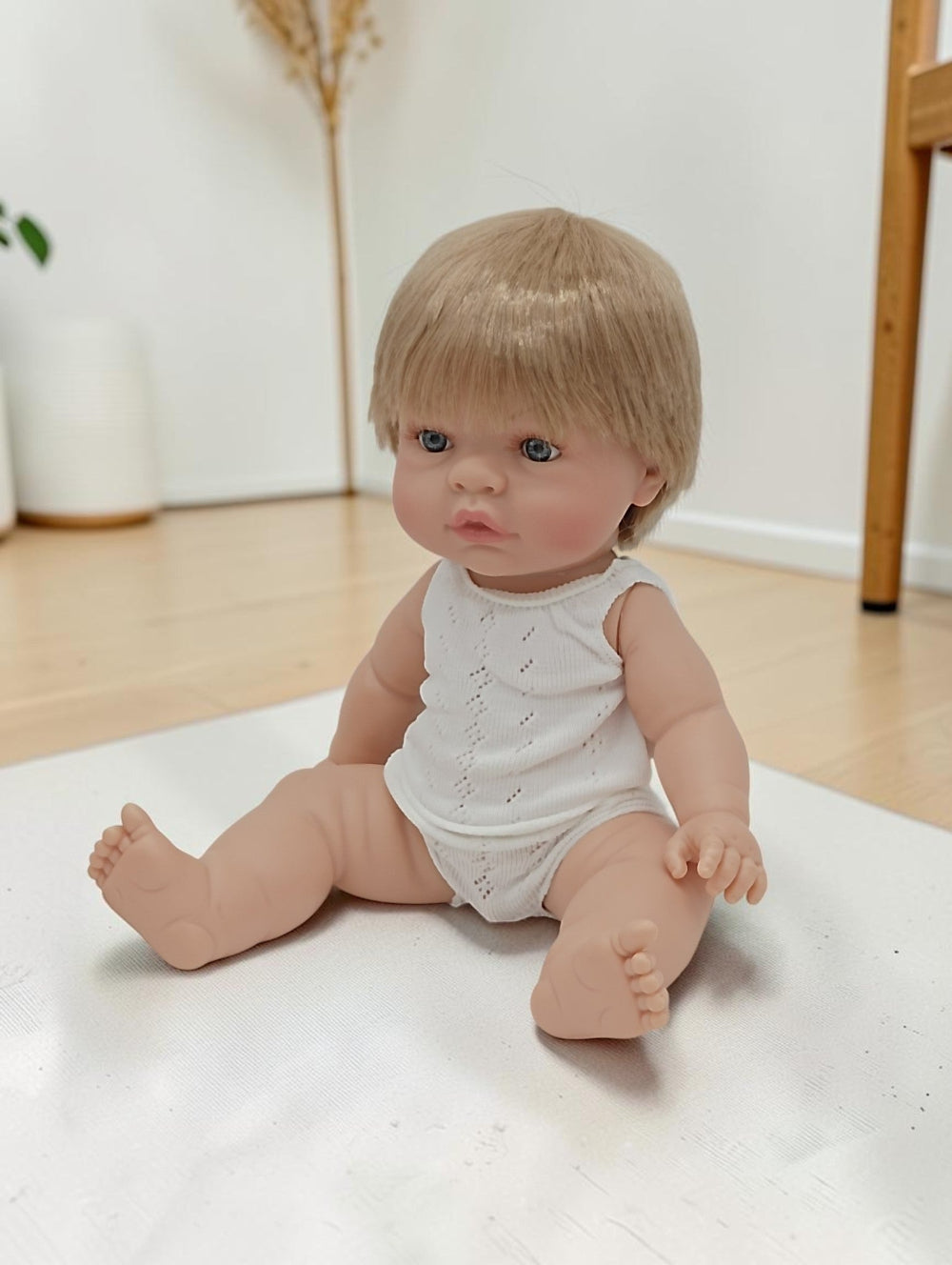 Baby doll with blonde hair and blue eyes sitting on a white surface.