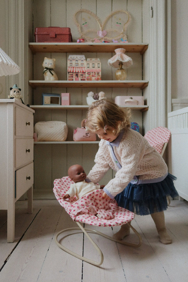 Child gently placing doll in rose bouncer during nurturing pretend play, developing empathy and care skills