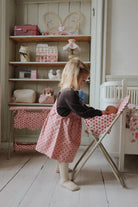 Child feeding doll in rose high chair during nurturing pretend play, demonstrating realistic mealtime scenarios