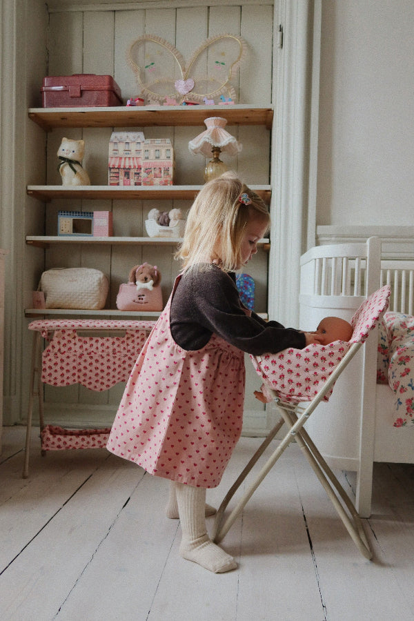 Child feeding doll in rose high chair during nurturing pretend play, demonstrating realistic mealtime scenarios