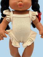 A close-up of a doll wearing a ribbed cream-colored romper with ruffled shoulder straps and a ruffled hem, shown against a plain light background.