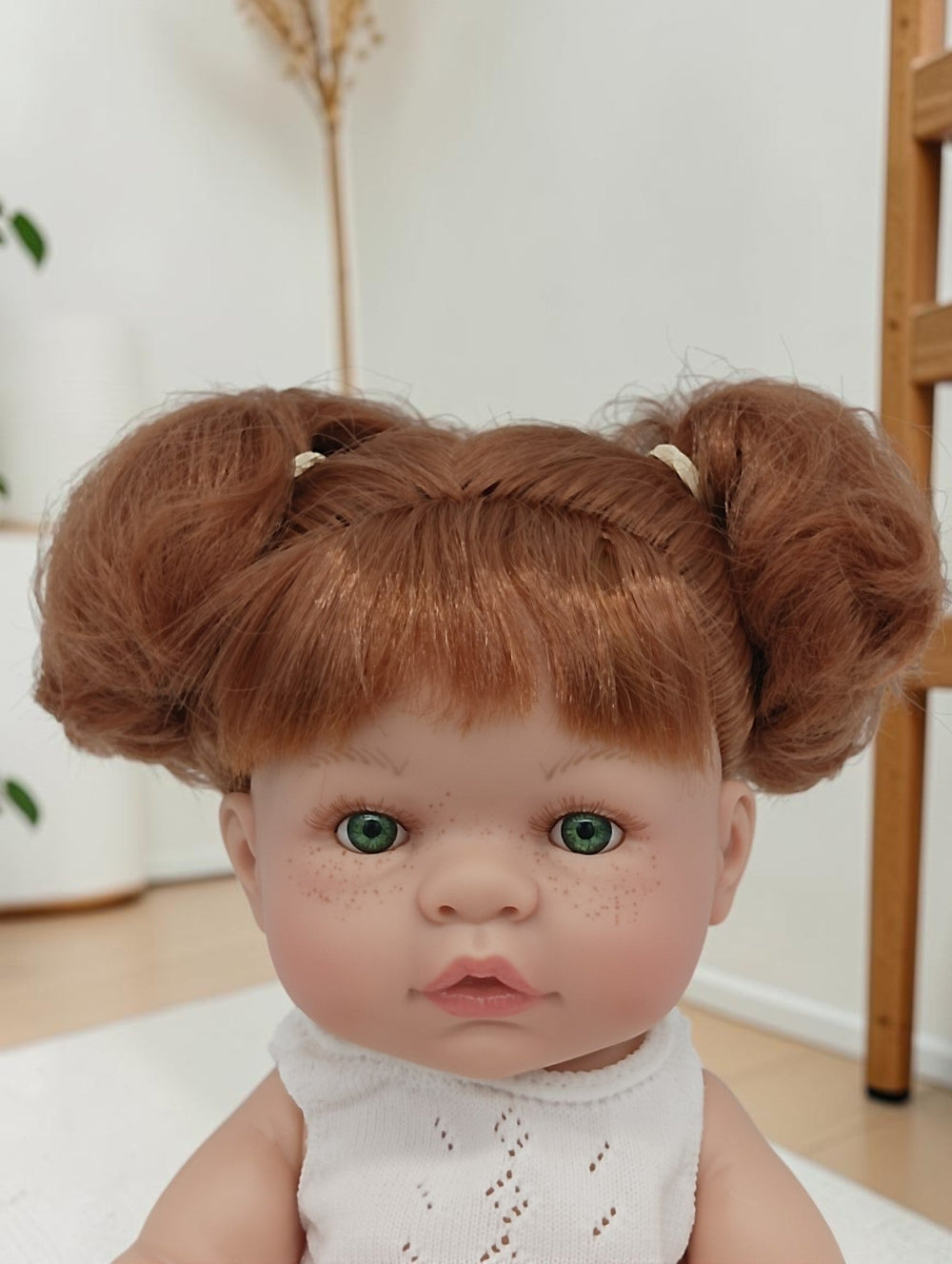 Doll with red hair styled in buns wearing a white outfit indoors.