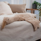 Cream Senger goose cuddly toy laying on knit blanket in modern bedroom setting