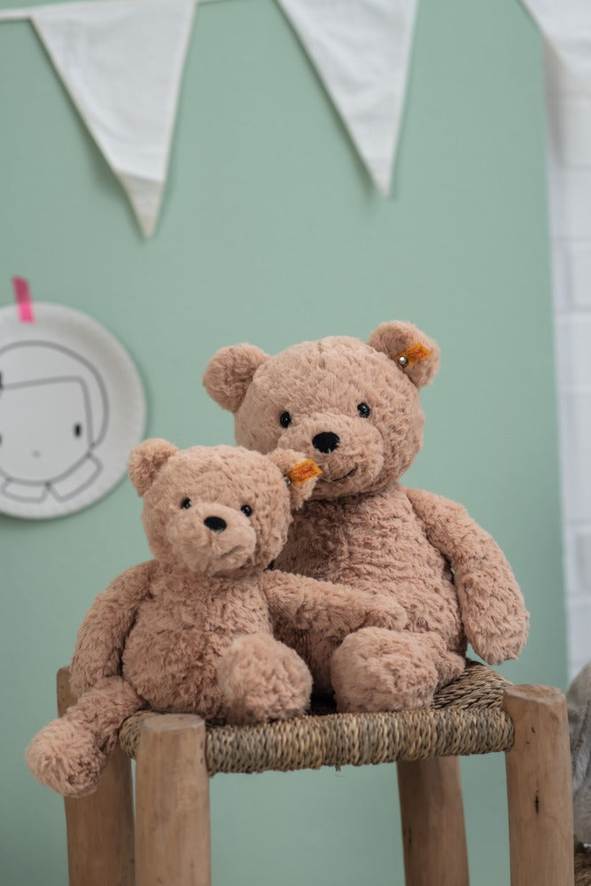 Two teddy bears sitting on a wooden stool against a light green wall.