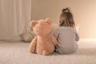 Child sitting on a bed with a large teddy bear, facing away from the camera.