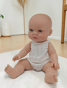 Baby doll wearing a white romper sitting on a light-colored surface.