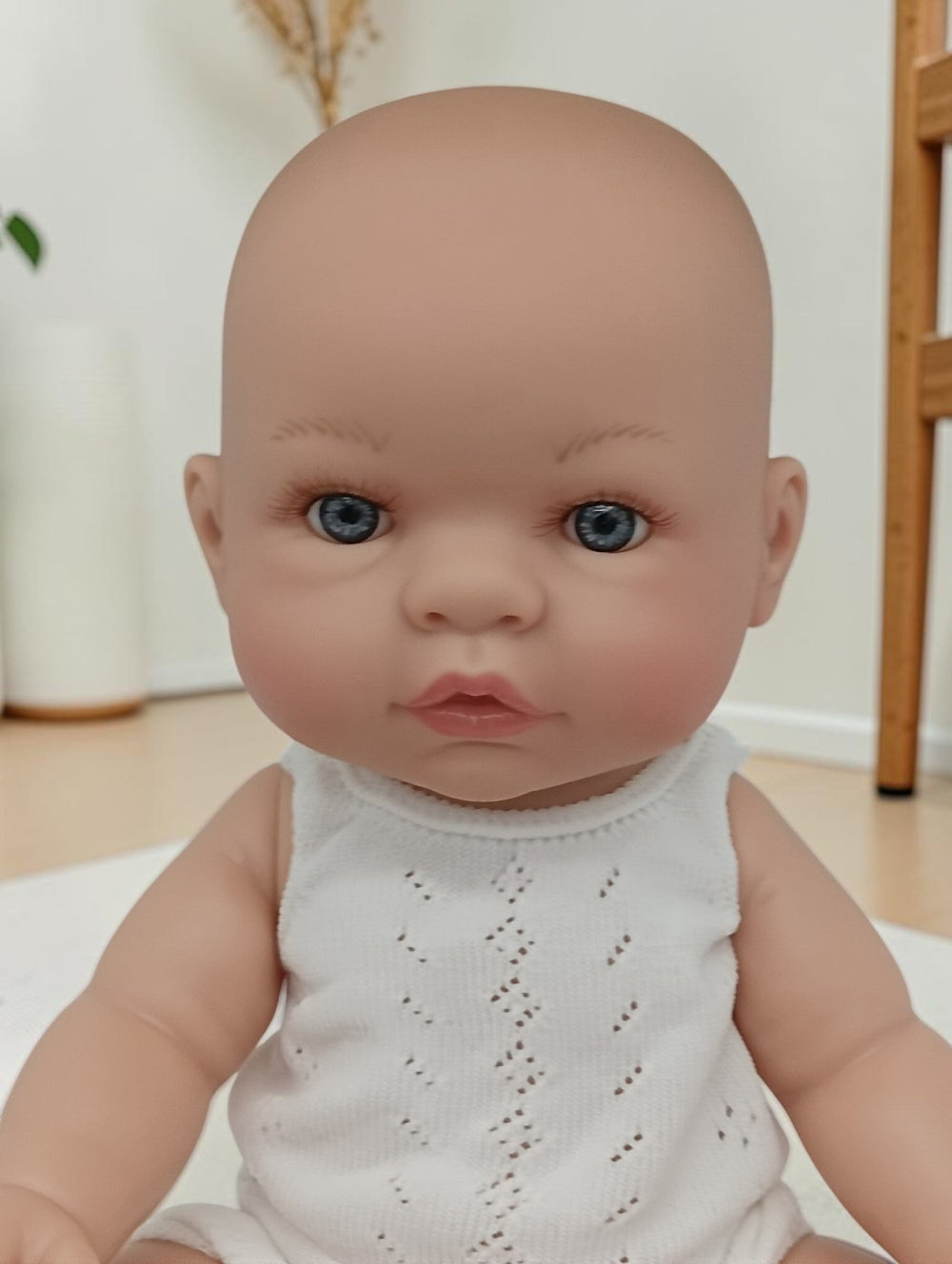 Realistic baby doll with blue eyes wearing a white outfit indoors.