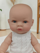 Realistic baby doll with blue eyes wearing a white outfit indoors.