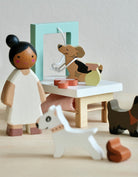 Wooden toy figures of a girl and a dog with a small table and other toys on a light background