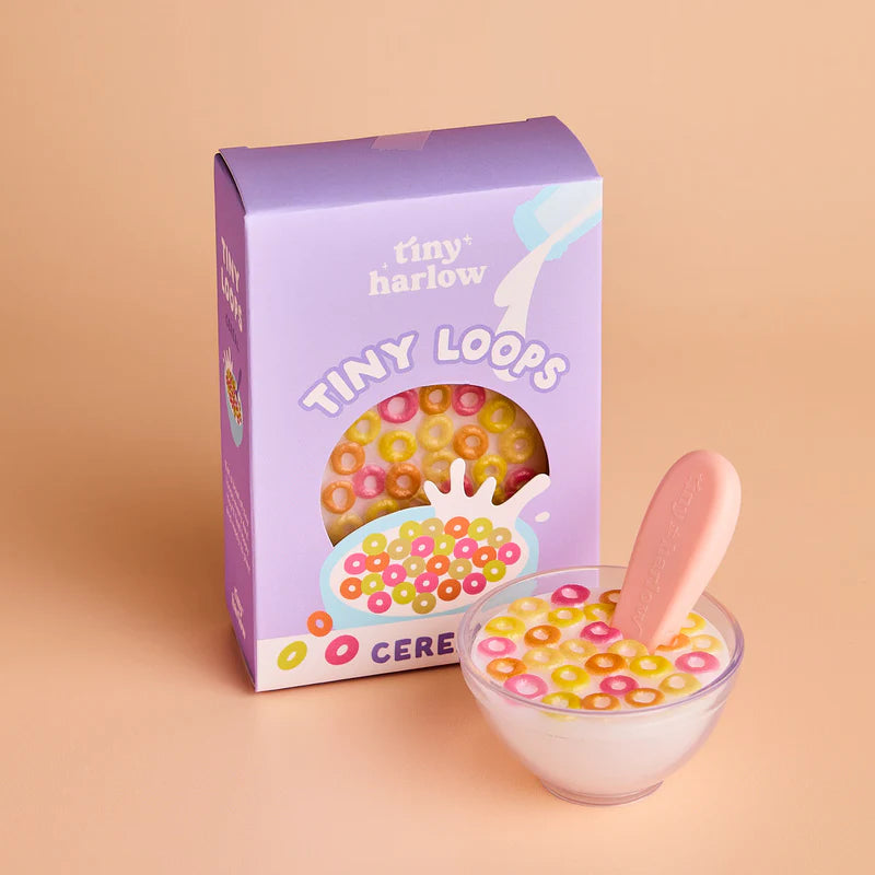 Box of 'tiny harlow' Tiny Loops cereal with a bowl of cereal and pink spoon on a beige background