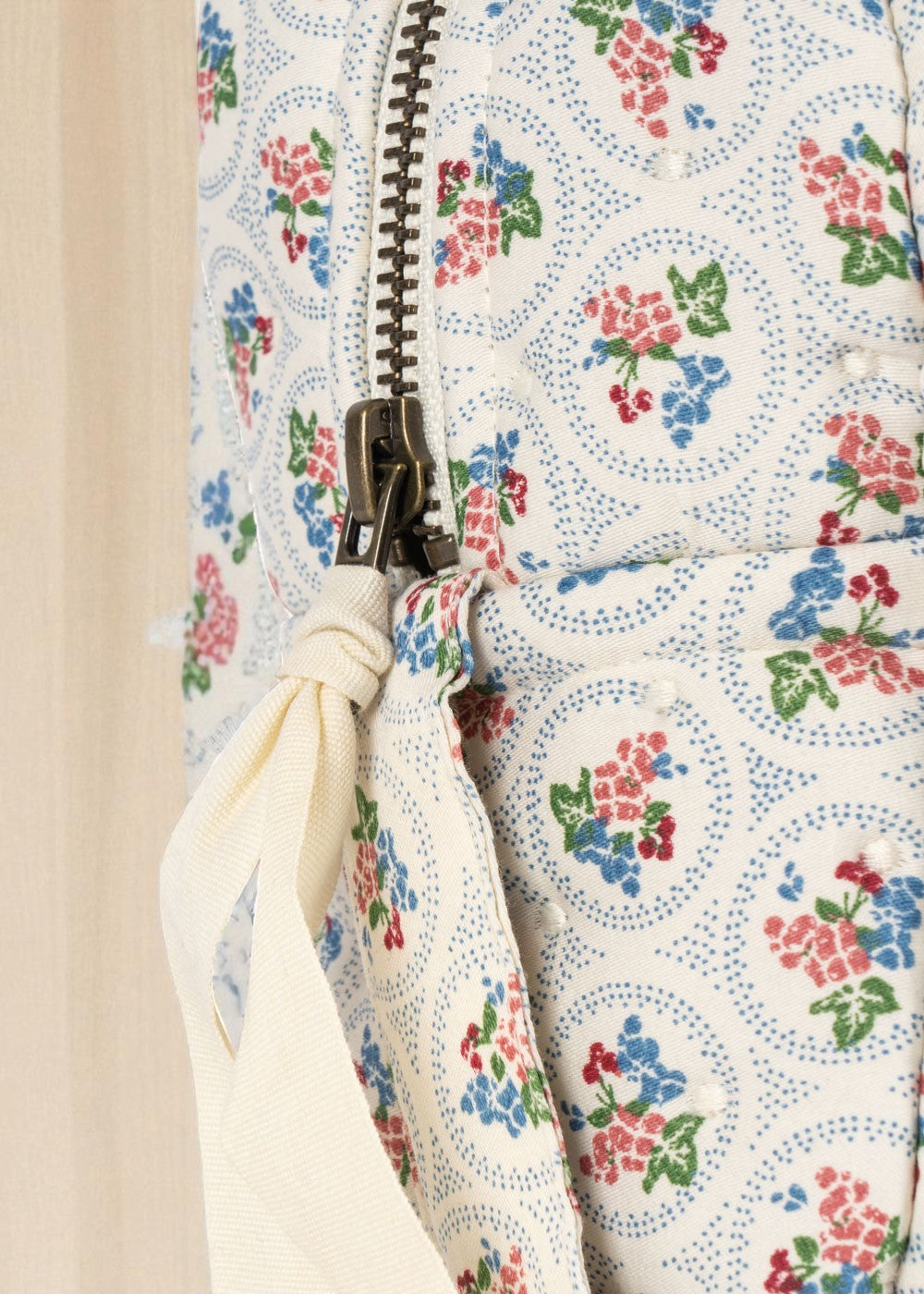 Close-up of bronze zipper with cream ribbon pull on floral patterned children's doll bag