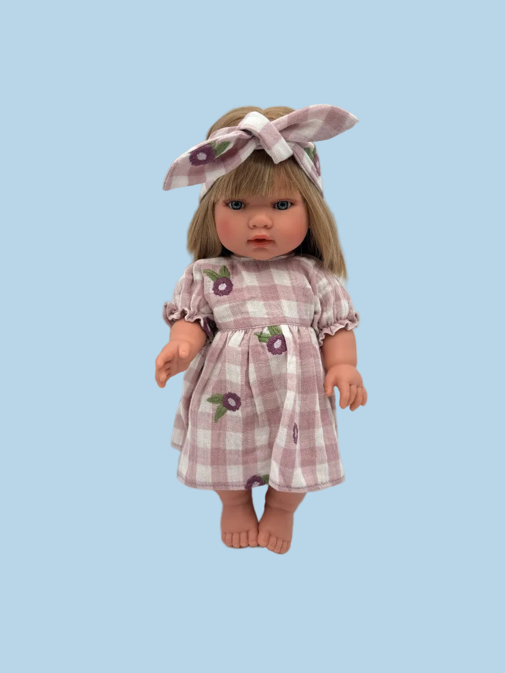 A doll with blonde hair wearing a purple and white gingham dress with flower motifs and a matching bow headband