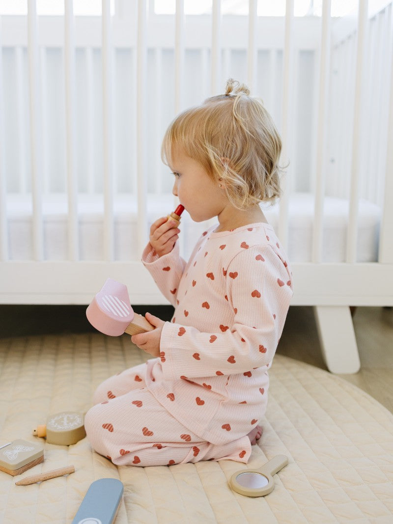 Child in a heart-patterned outfit sitting on the floor with toys around
