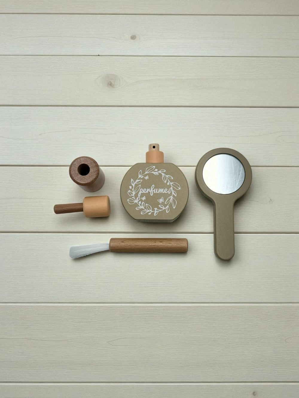 Set of wooden beauty products including a perfume bottle, brush, and mirror on a light wooden surface.
