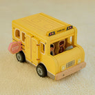 Close-up of wooden student and driver figures with warm hand-painted illustrations standing beside yellow school bus